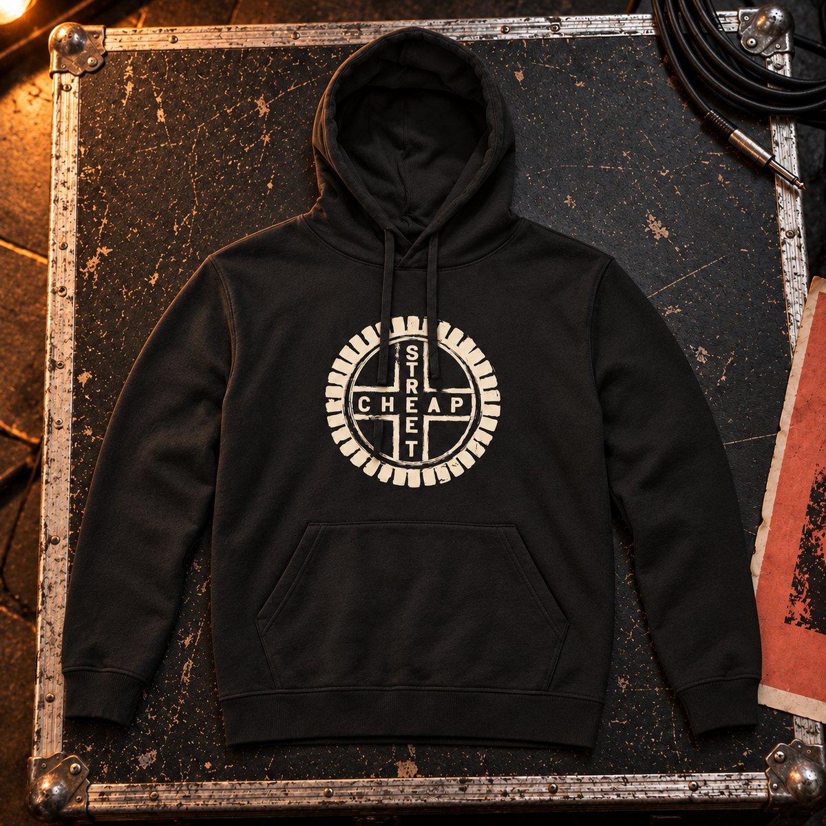 Cheap Street logo hoodie in black with the warm cream Cheap Street emblem on the chest, laid on a flight case