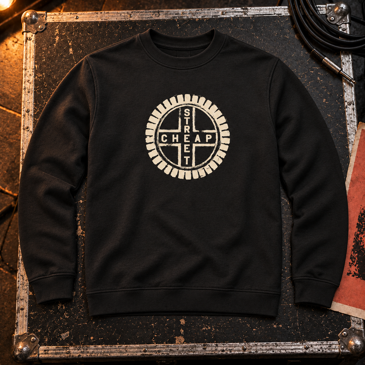 Cheap Street logo sweatshirt in black with the warm cream Cheap Street emblem on the chest, laid on a flight case