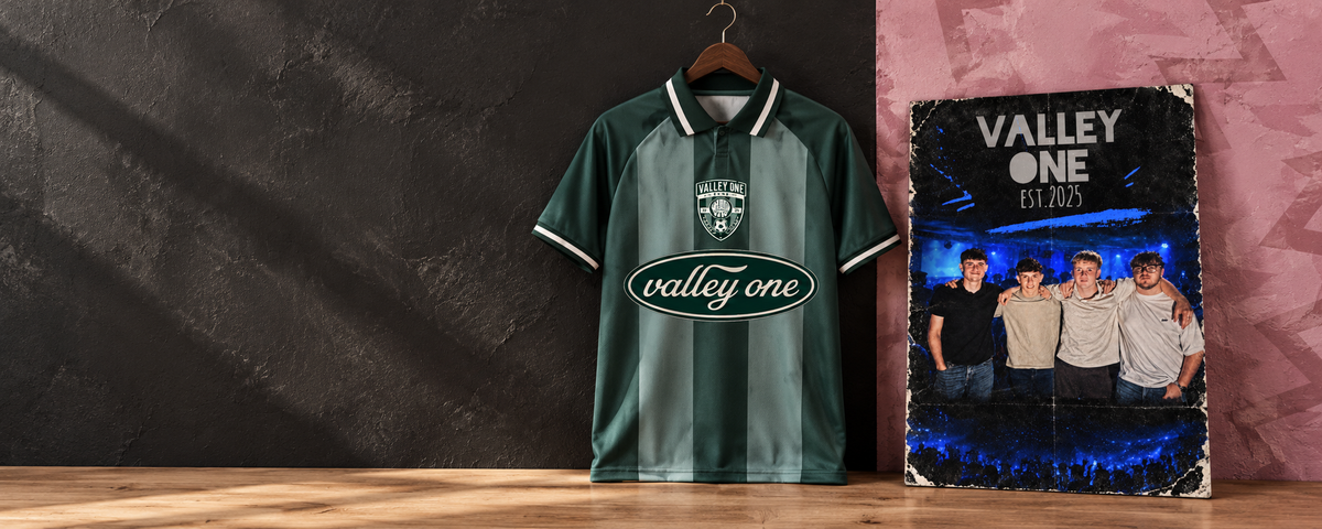 A green striped Valley One football shirt on a hanger beside the blue and black Valley One poster, against charcoal and pink walls