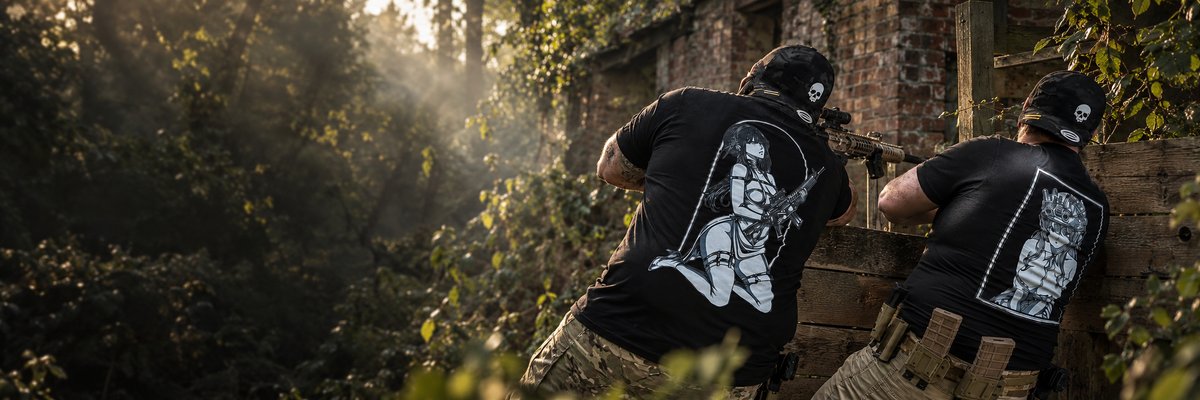 Two airsoft players wearing black N.O.C. graphic T-shirts beside a timber barricade.