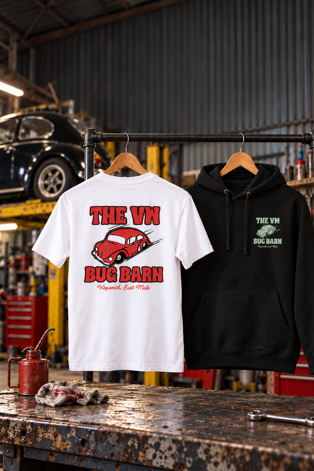 A white Bug Barn T-shirt with the red Beetle back print and a black Bug Barn hoodie hanging on a rail in a VW workshop