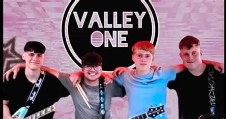 The four members of Valley One in front of a pink backdrop with the band's circular sign