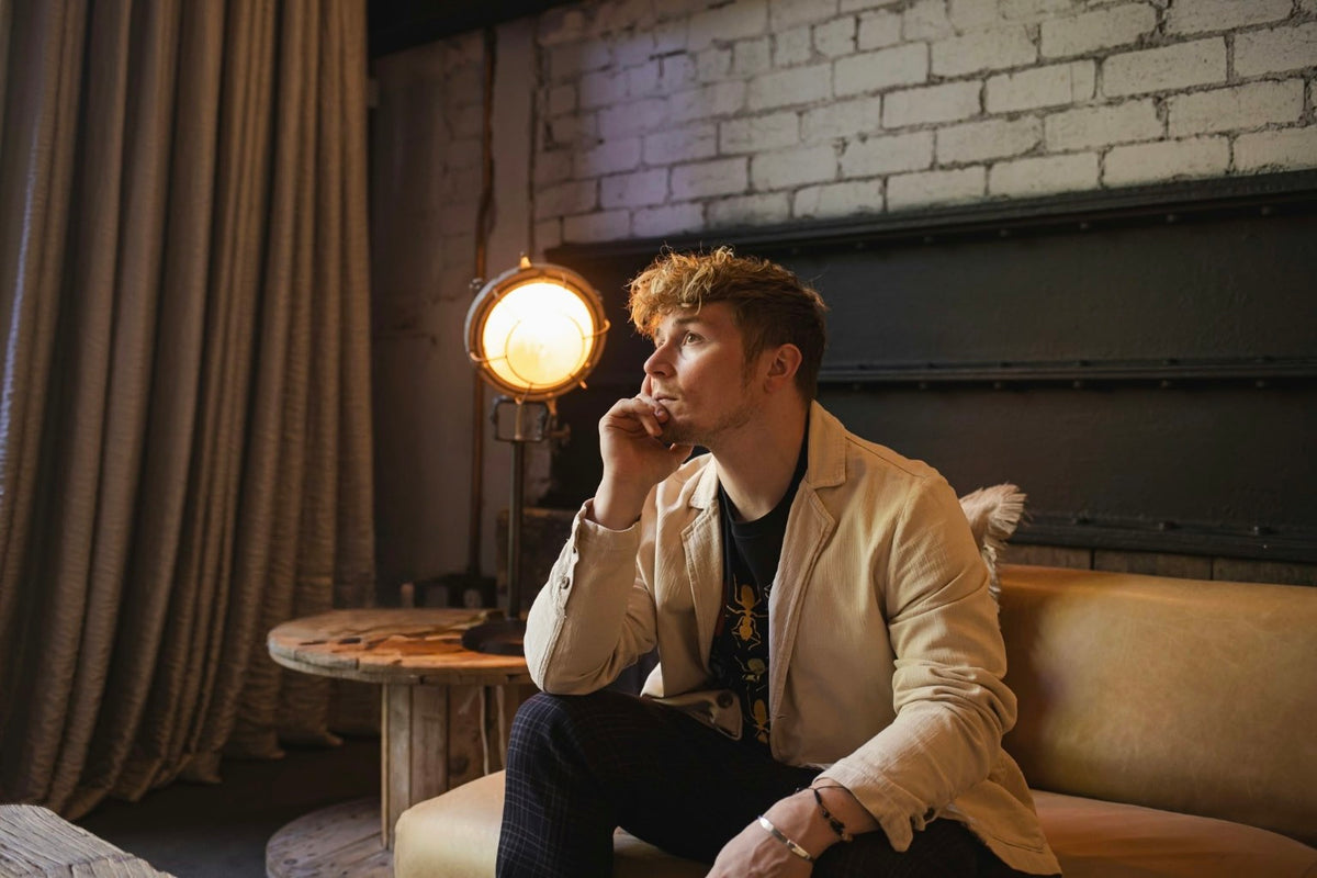 Kuill seated on a tan leather sofa, hand at his chin, beside an amber studio lamp
