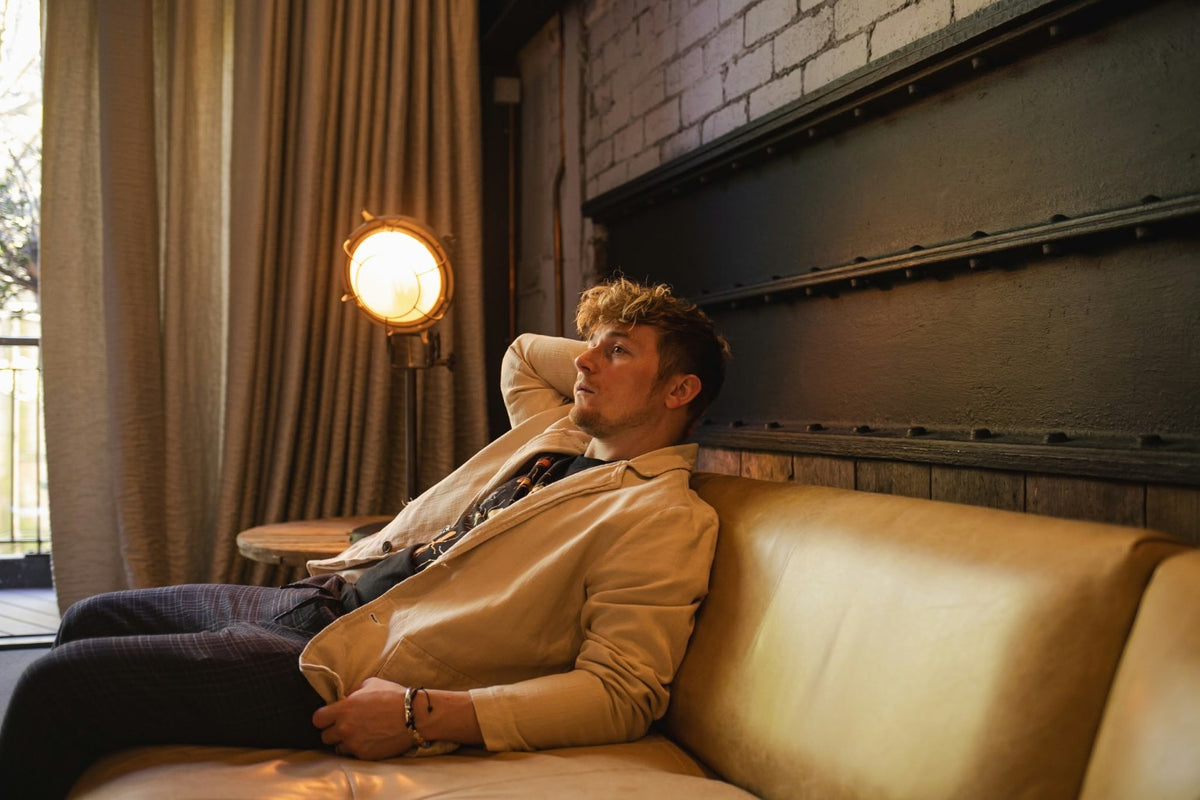 Kuill reclining on a tan leather sofa beside a glowing amber studio lamp
