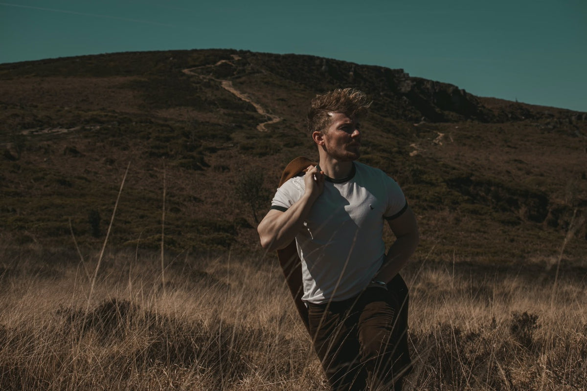 Kuill on an autumn moor with his coat over his shoulder, under a teal sky